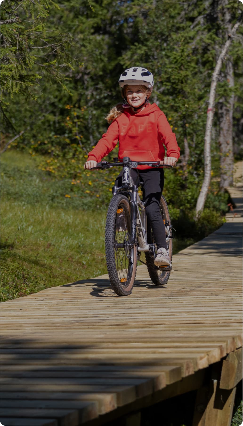 Child in a red hoodie and helmet rides a bicycle.