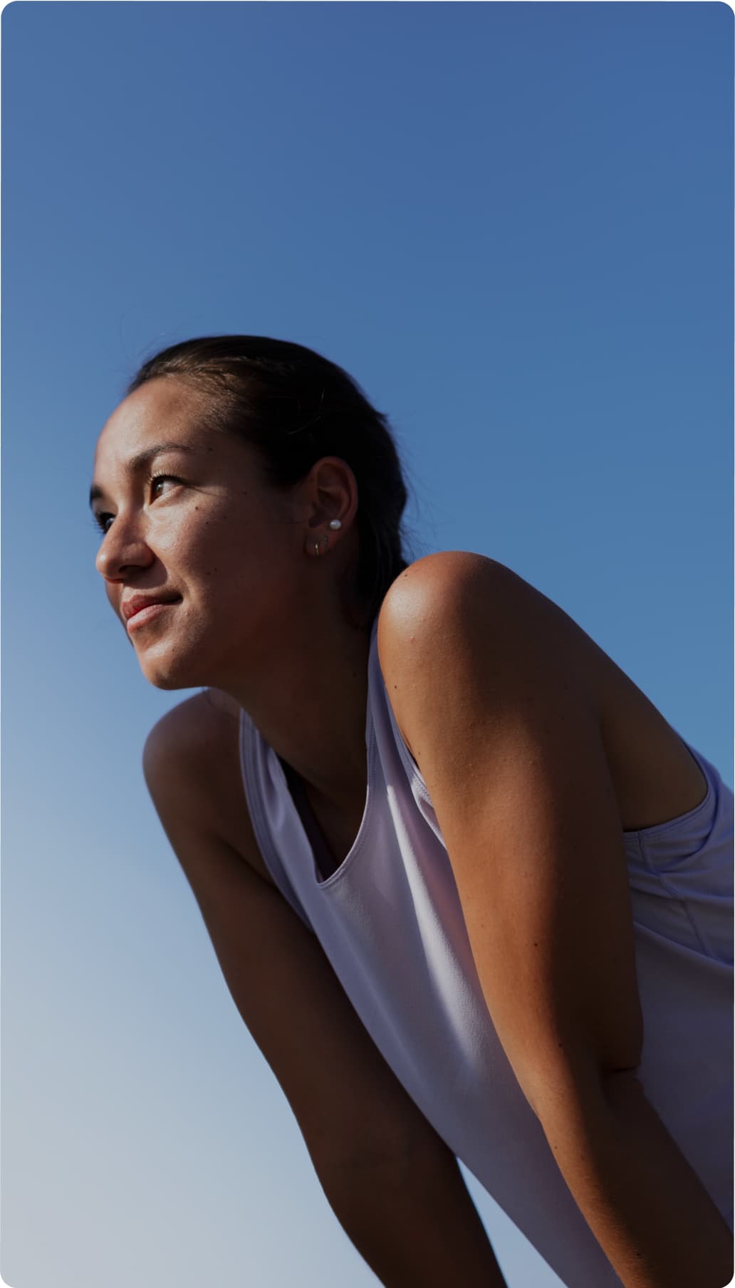 Woman in a sleeveless top leans forward, looking into the distance against a clear blue sky.
