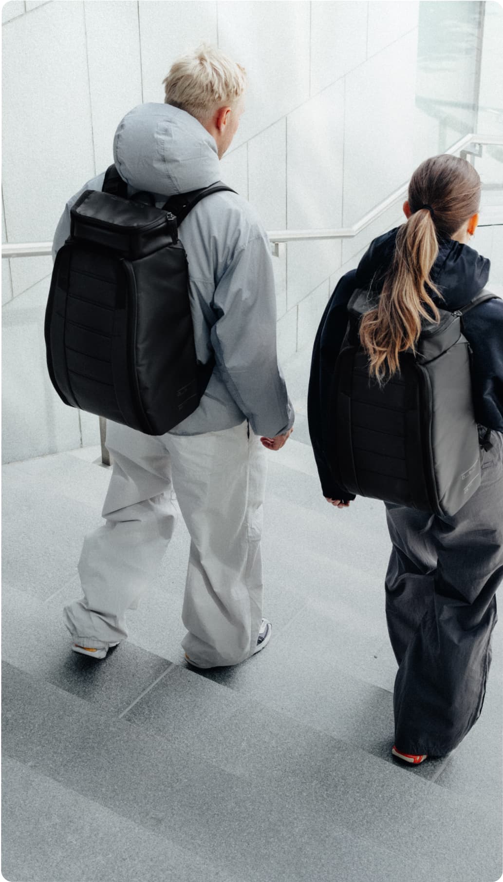 Two people with black backpacks walk down concrete stairs.