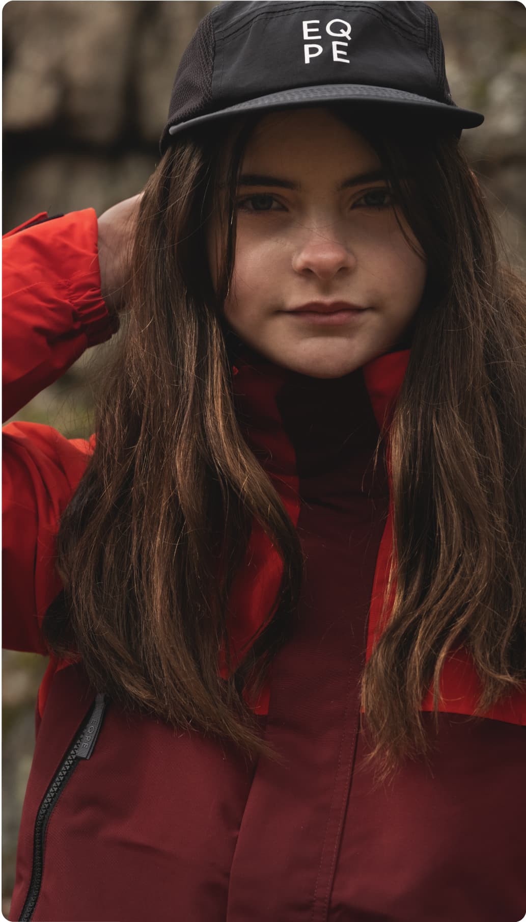 Young girlwearing a black cap and red jacket.