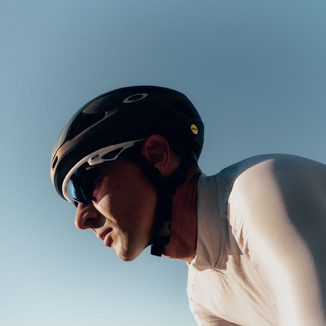 Cyclist wearing a black helmet and sunglasses under a clear blue sky.