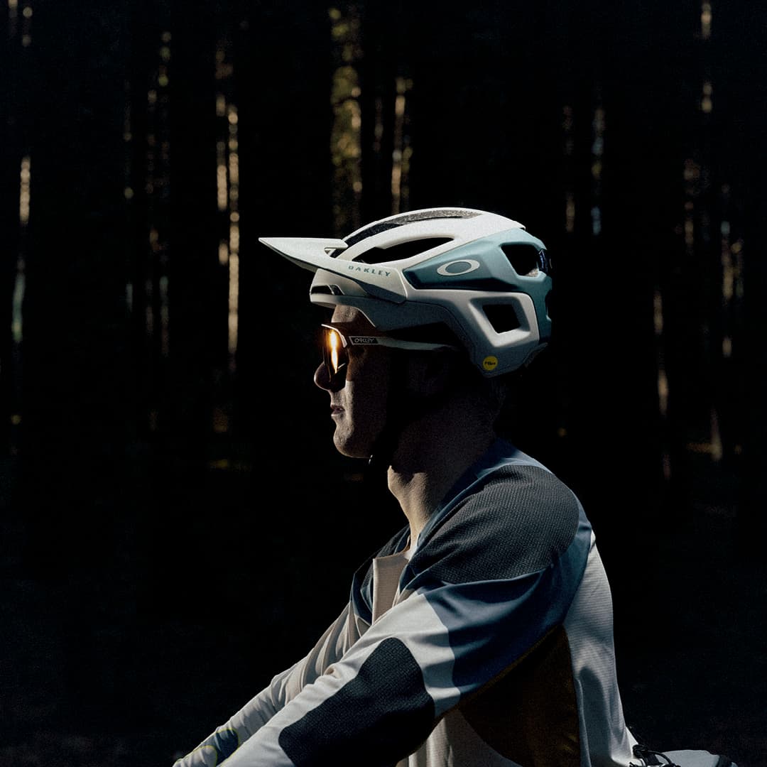 A person wearing a helmet and sunglasses with sunlight casting shadows on their face.