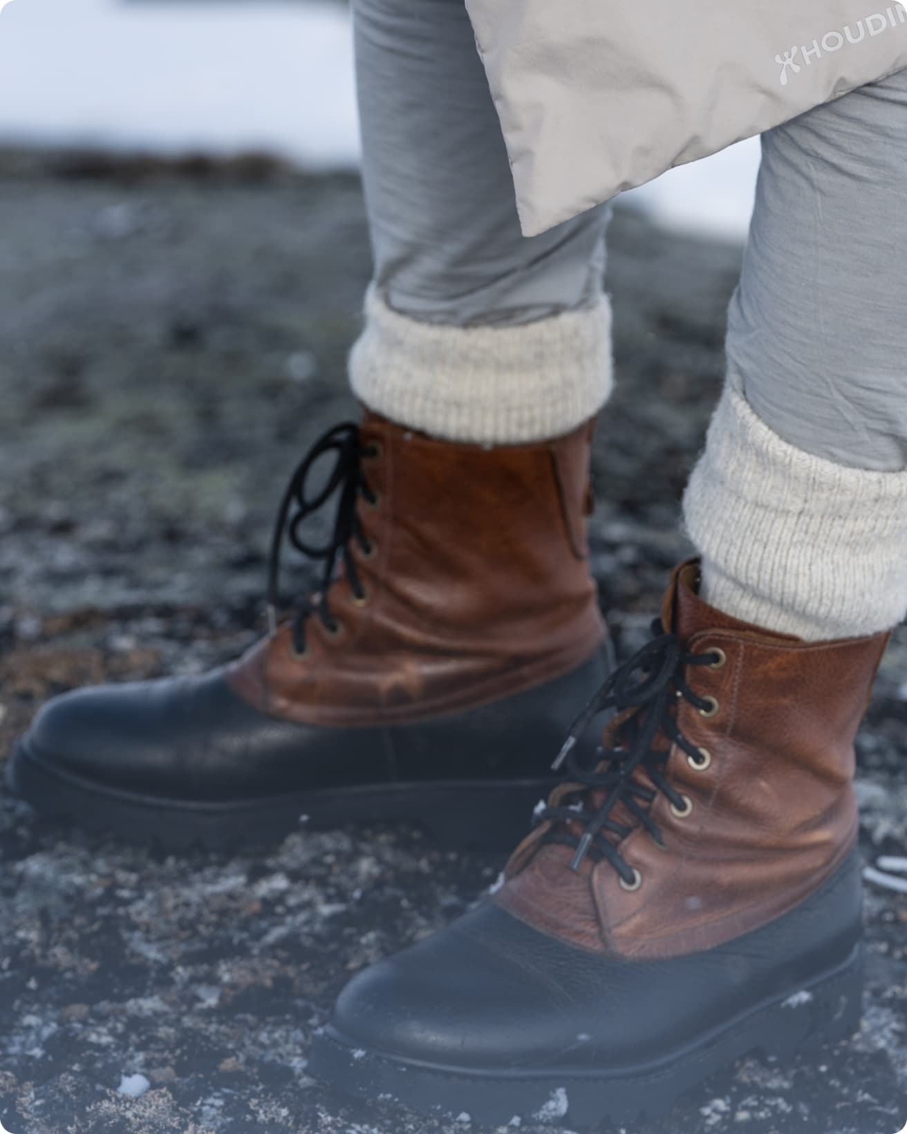 Close-up of a person wearing brown and black lace-up boots with thick white socks, standing on rocky ground.