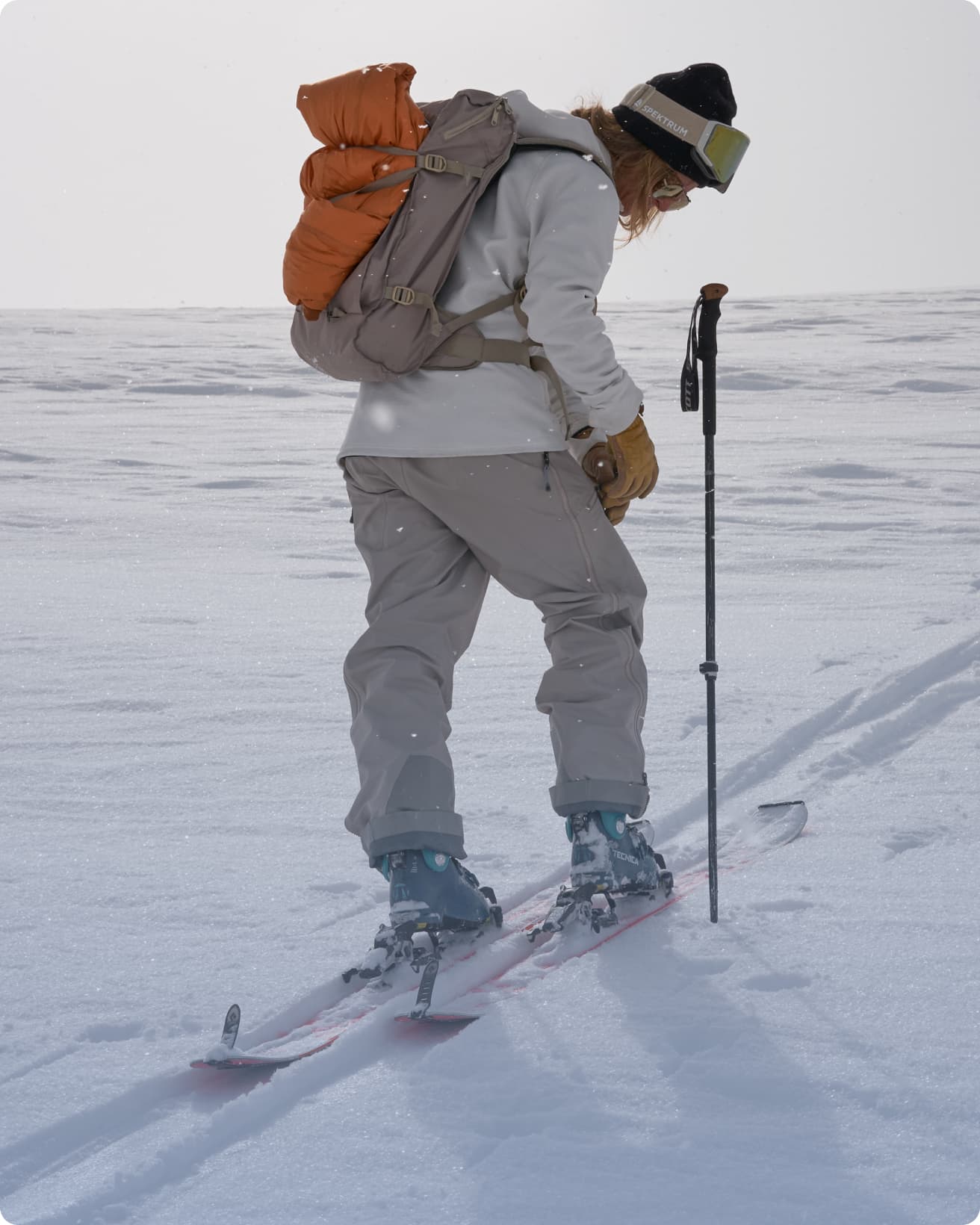 A skier in winter gear and a backpack, looking down and closing her pocket.