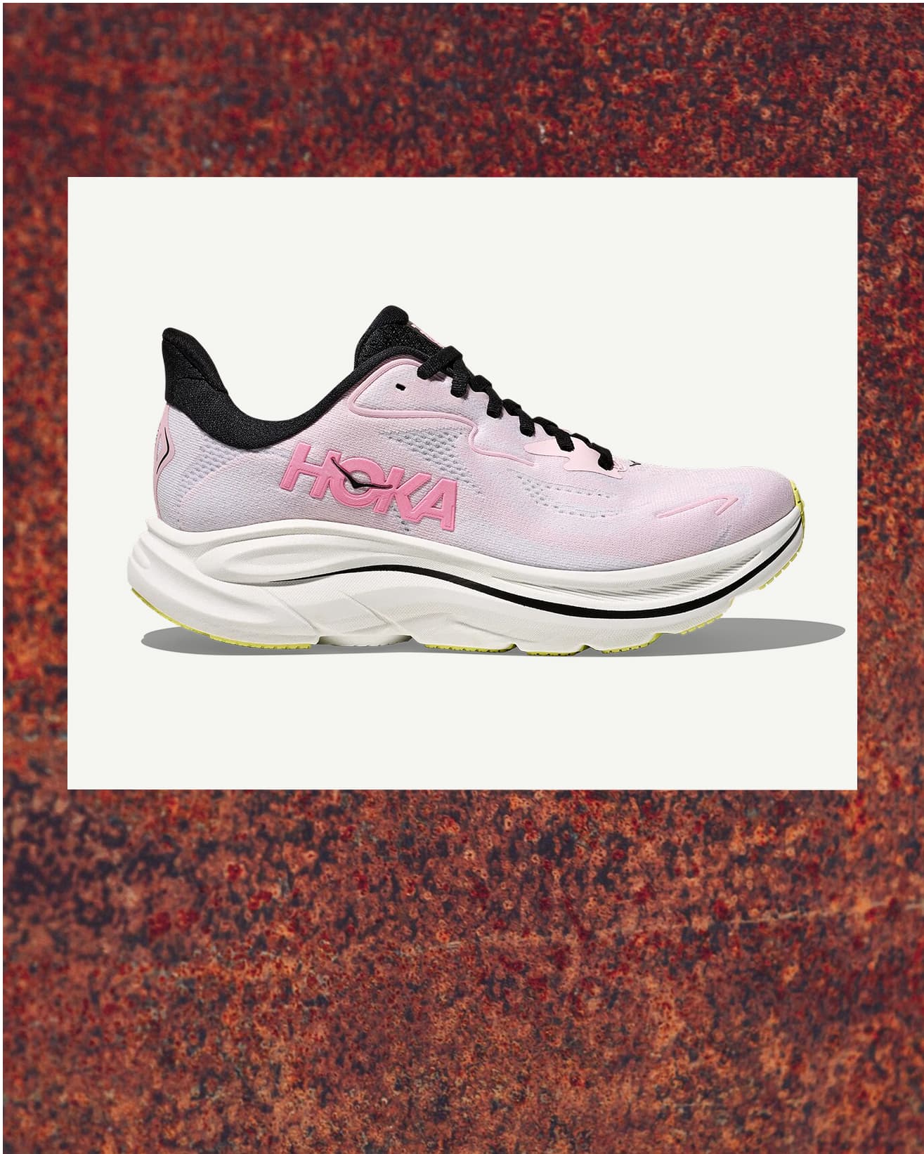 Pink and black running shoe with a white sole, displayed against a textured rust-colored background.