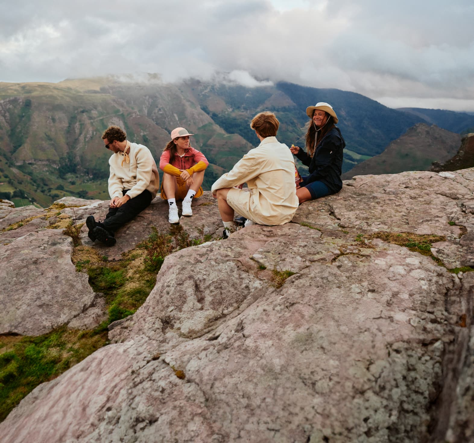 Four people sitting on a rock, dressed in casual outdoor attire.