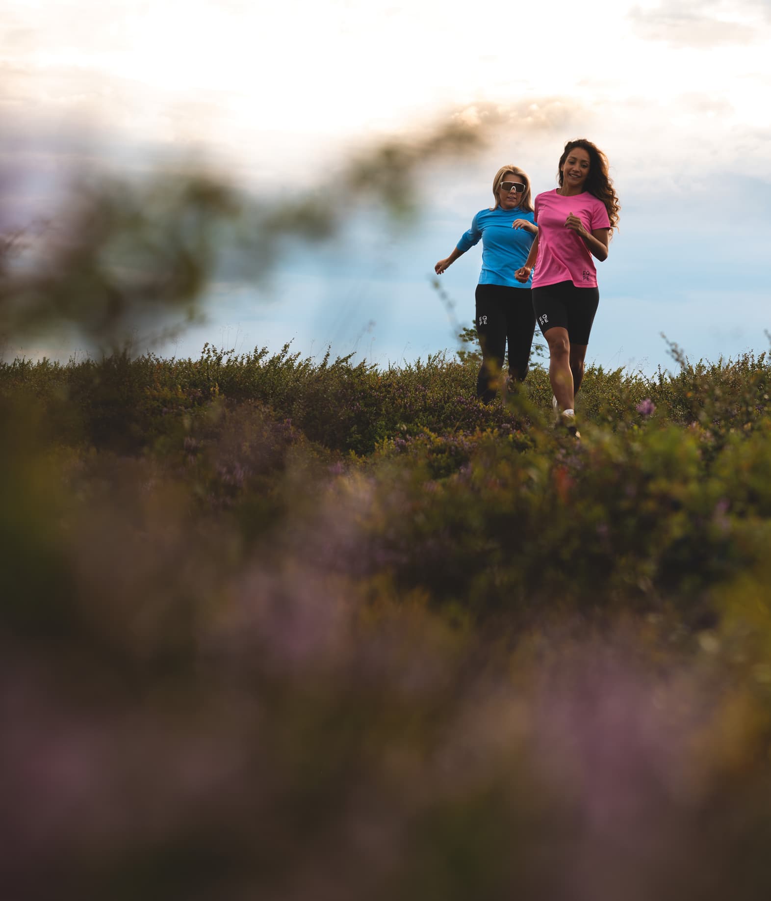Two women jogging on a trail surrounded by greenery.