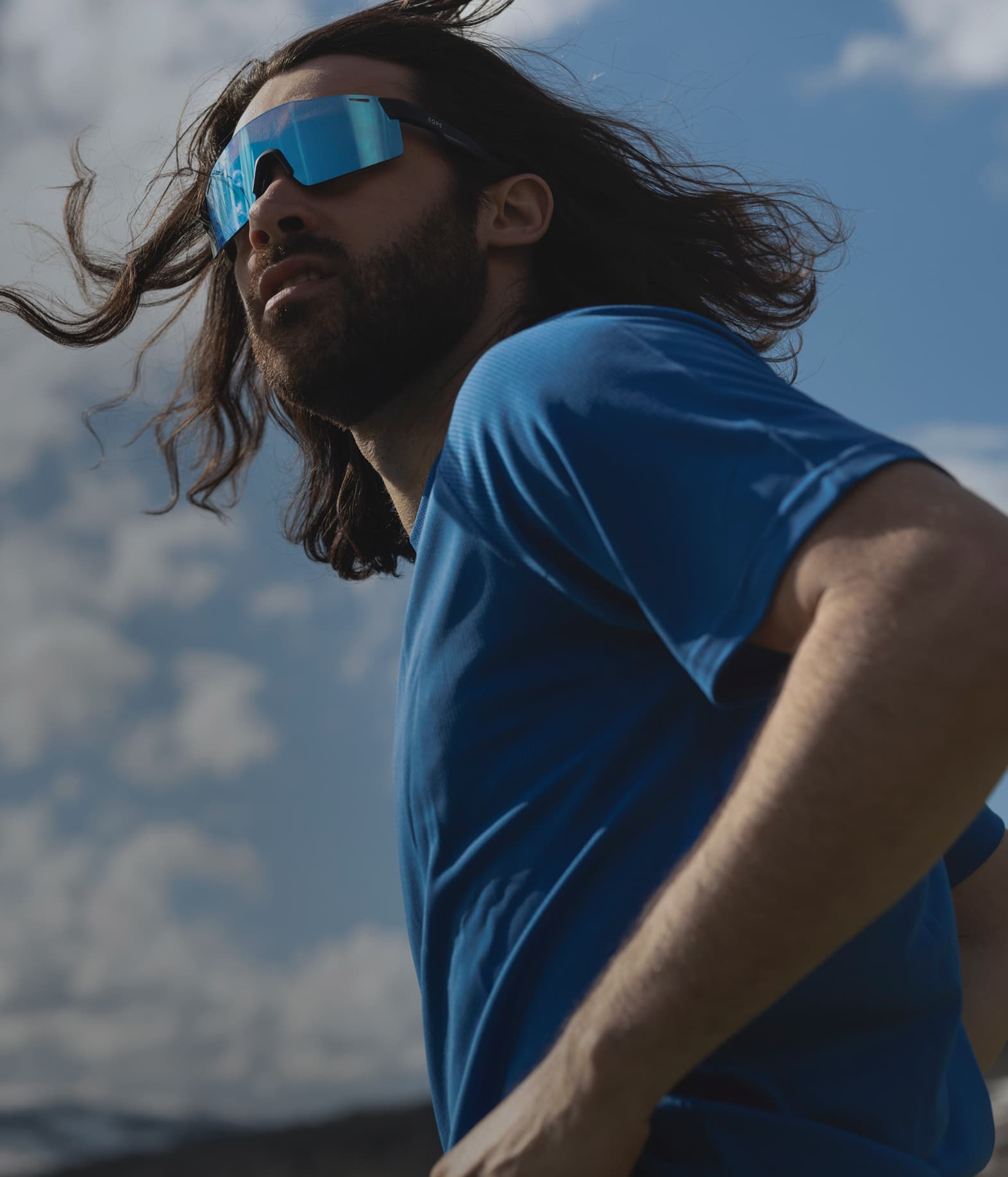 A person wearing reflective sunglasses and a blue T-shirt looks into the distance.