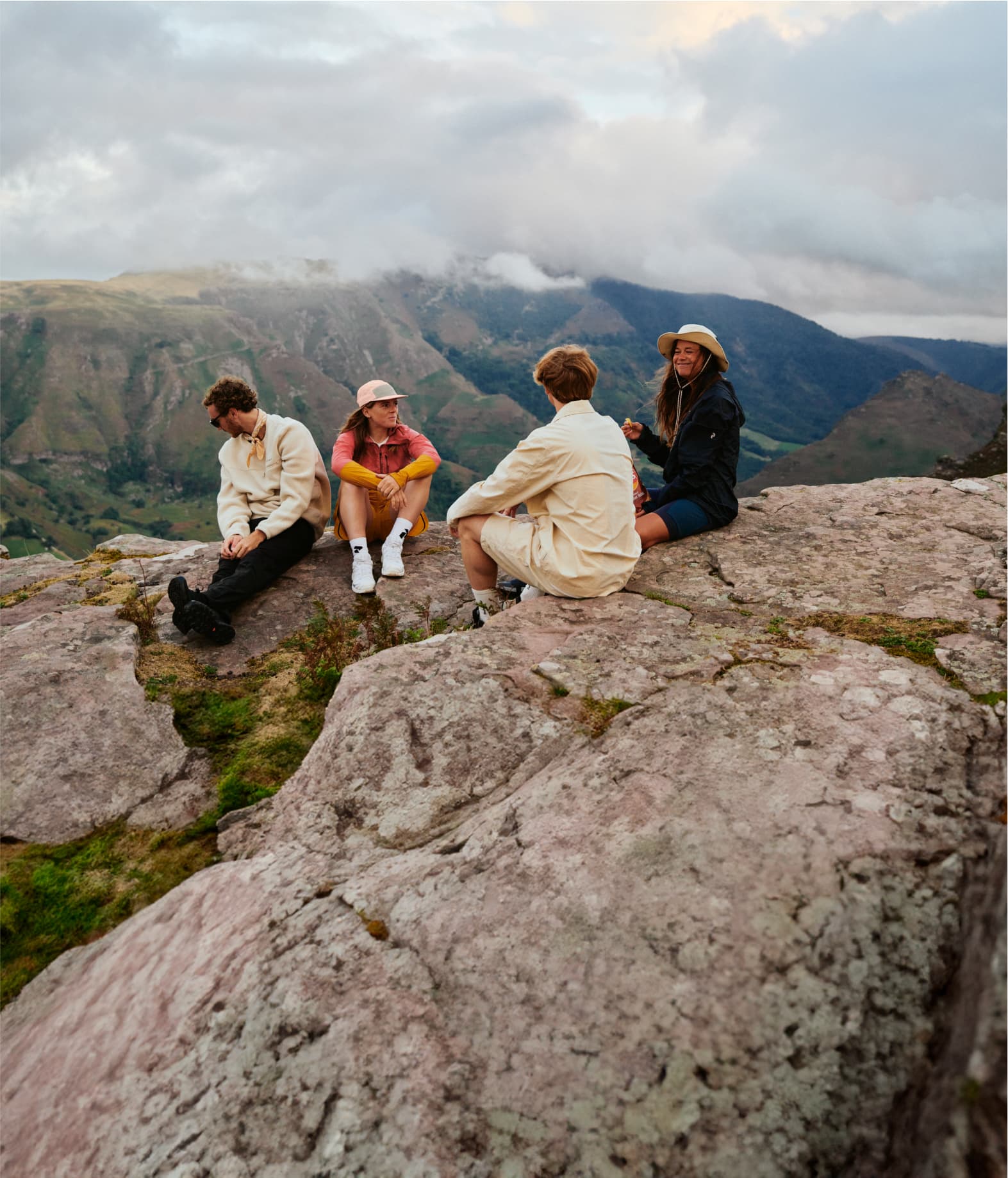 Four people sitting on a rock, dressed in casual outdoor attire.