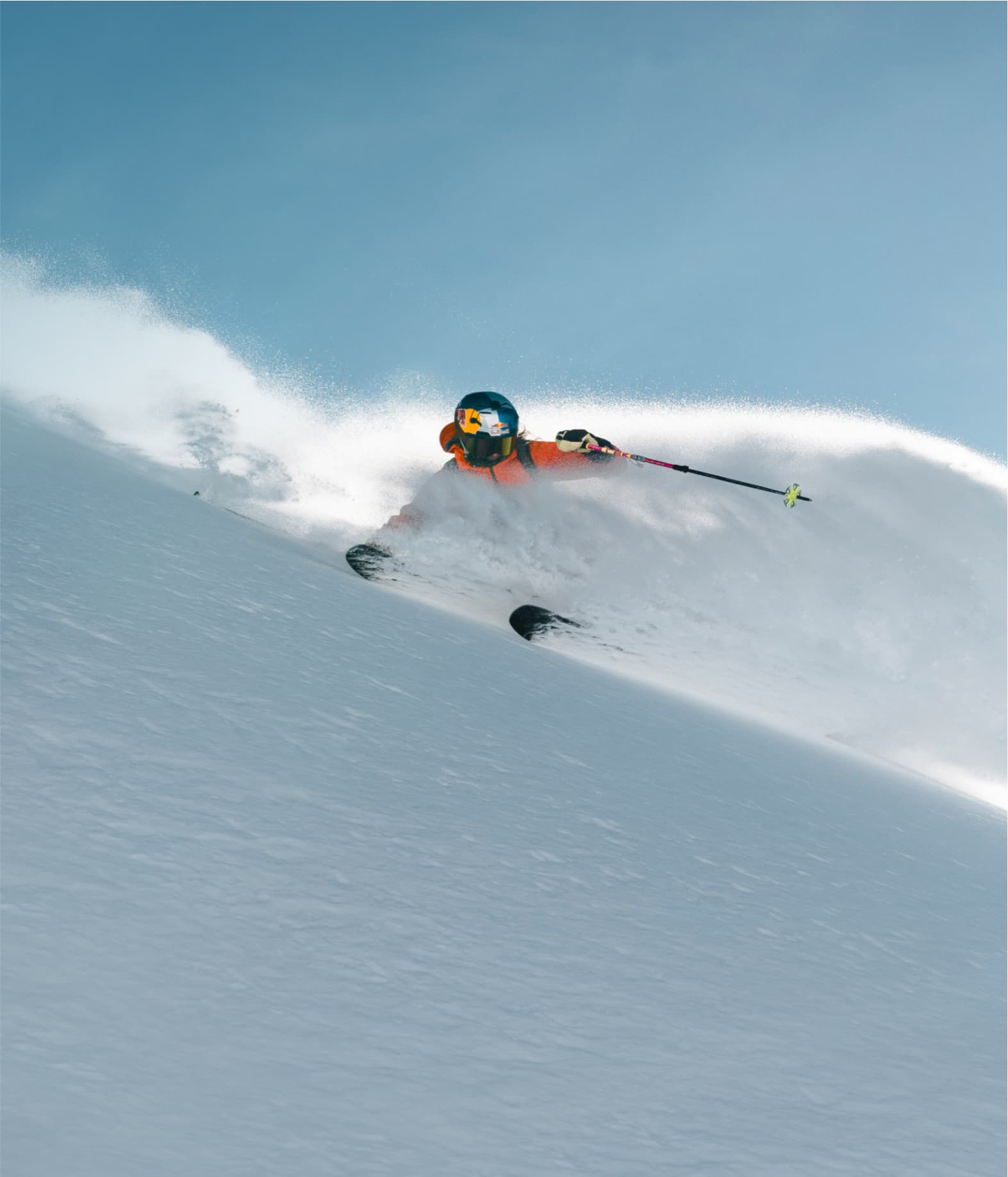 Skier in an orange jacket skiing through deep powder snow.