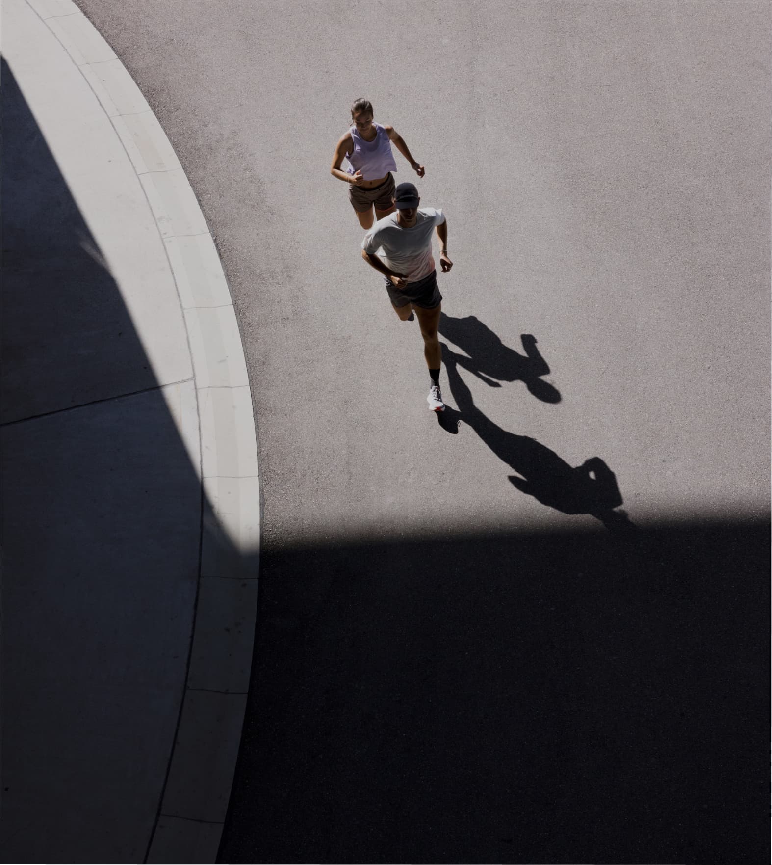 Two people jogging on a sunlit street, casting long shadows.