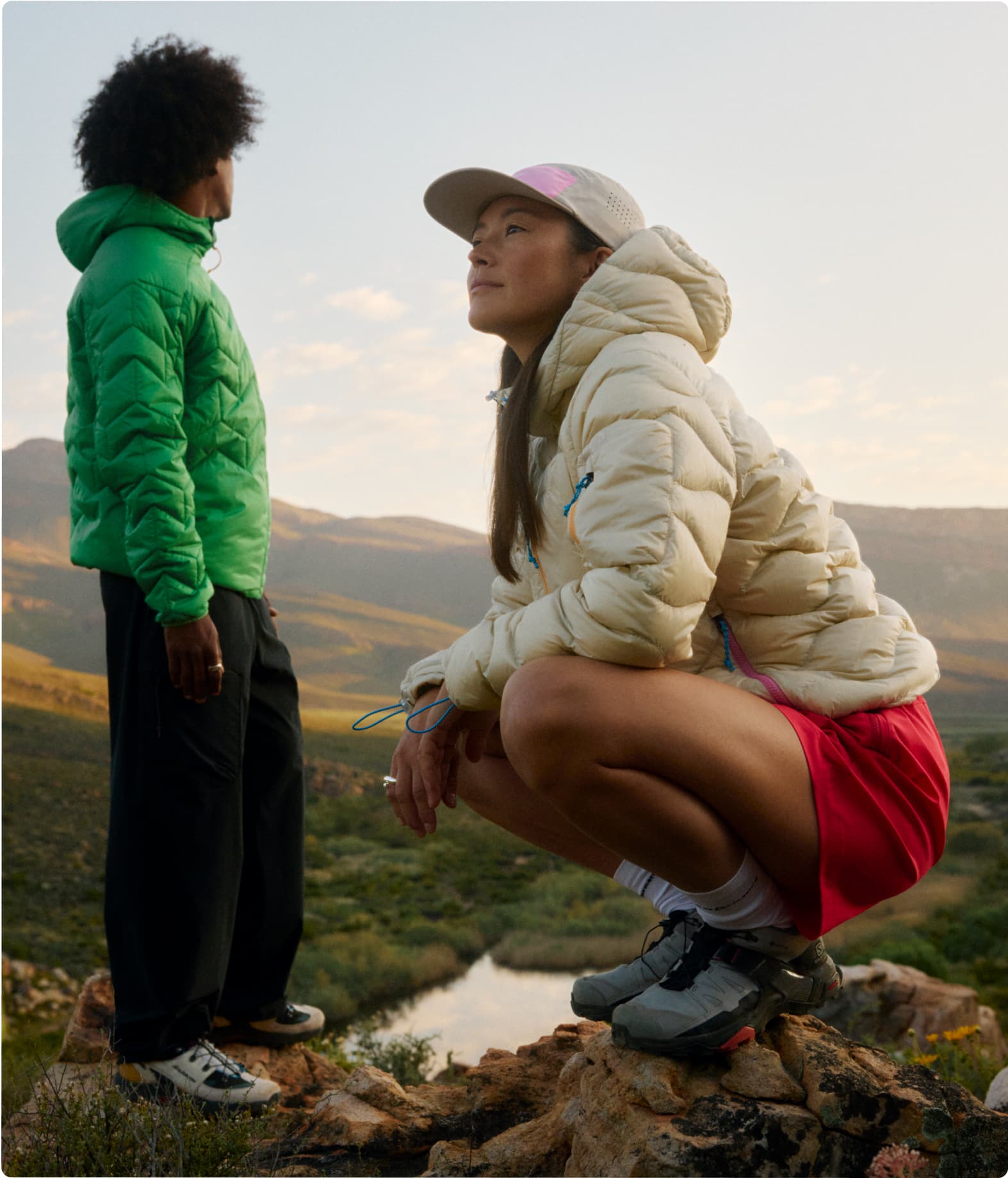 Two people in light weight jackets enjoy a scenic view, surrounded by mountains.
