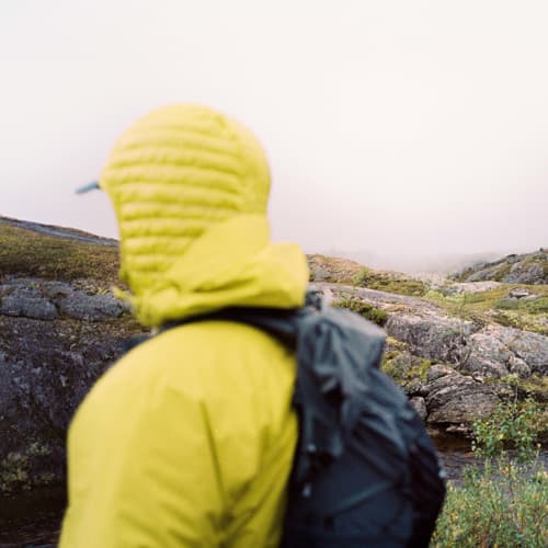 A person from behind wearing a yellow jacket in mountain terrain