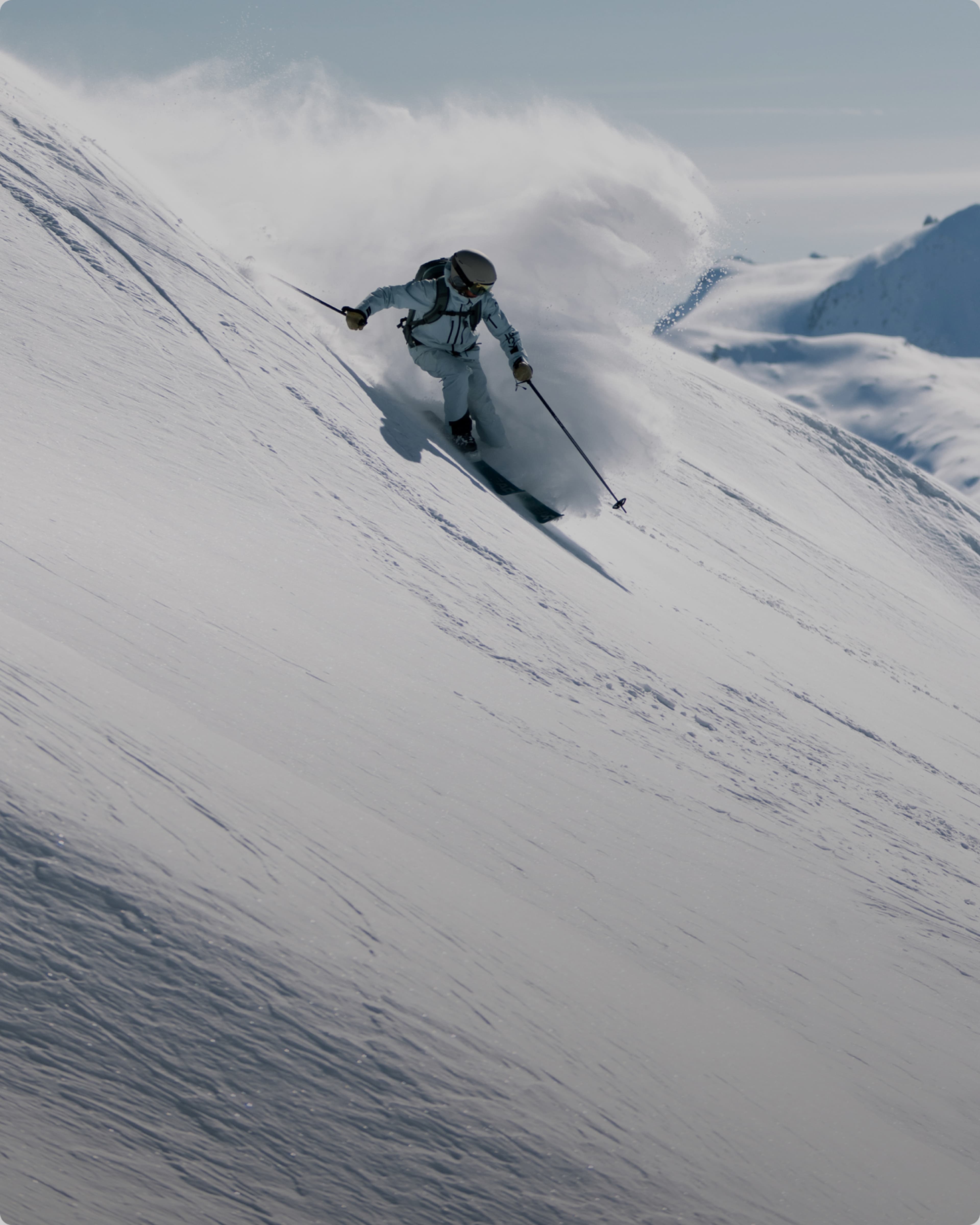 Skier carving down a steep, snowy slope, creating a spray of snow.
