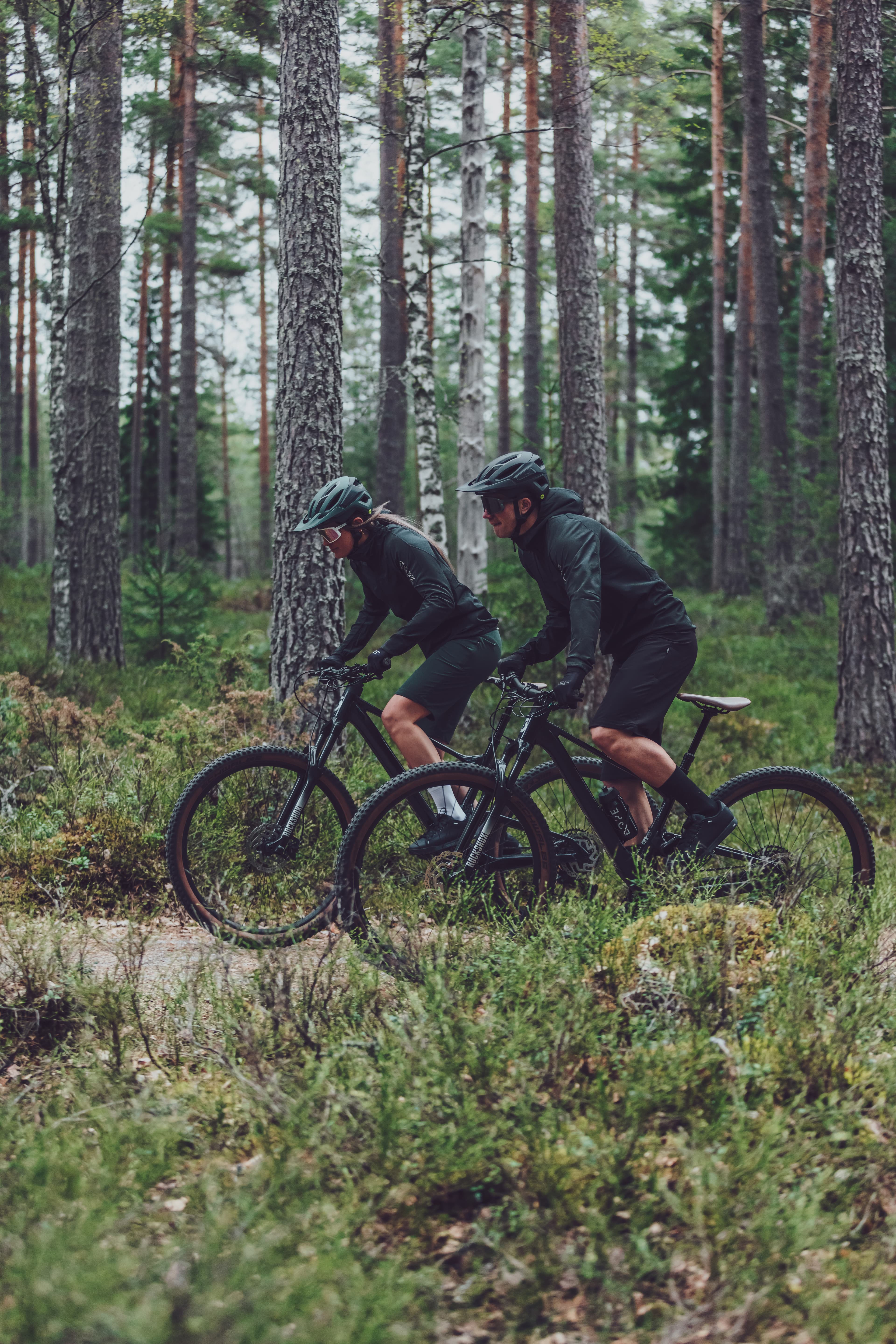 A man and a woman on mountain bikes riding thorugh a green forest