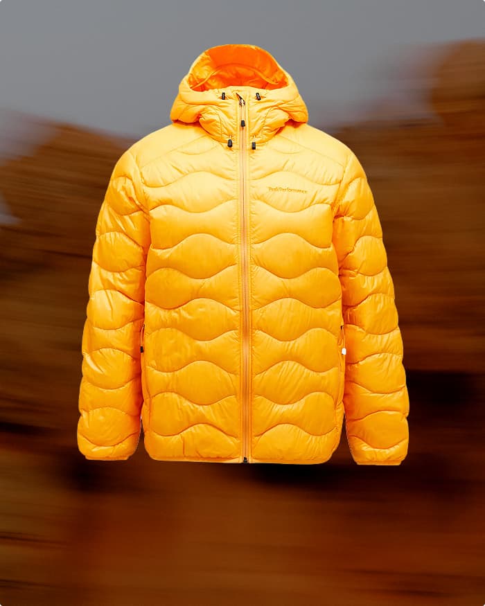 Bright orange puffer jacket with a hood, featuring wave-like stitching and a front zipper, set against a blurred brown background.
