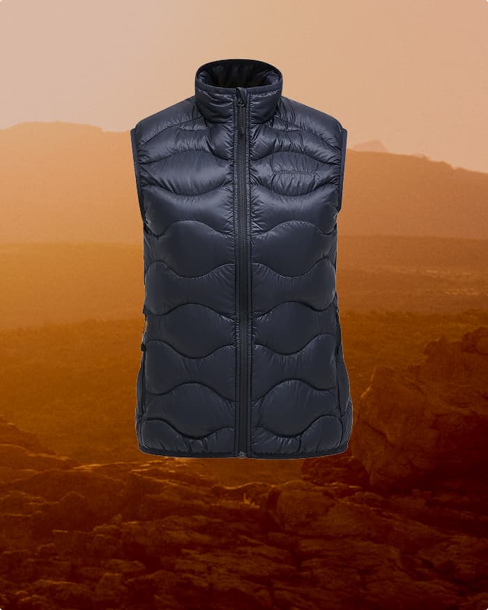A blck puffer vest with a high collar and wavy stitching, displayed against a warm, rocky landscape at sunset.
