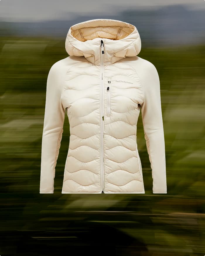Cream-colored quilted jacket with a hood and front zipper, displayed against a blurred green background.