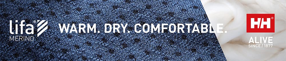 Close-up of a textured blue fabric with the text "lifa merino, WARM. DRY. COMFORTABLE." and "HH ALIVE SINCE 1877" logo on the right.