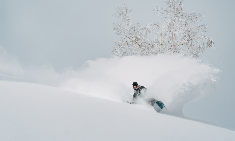 Snowboarder carving through fresh powder on a snowy slope.