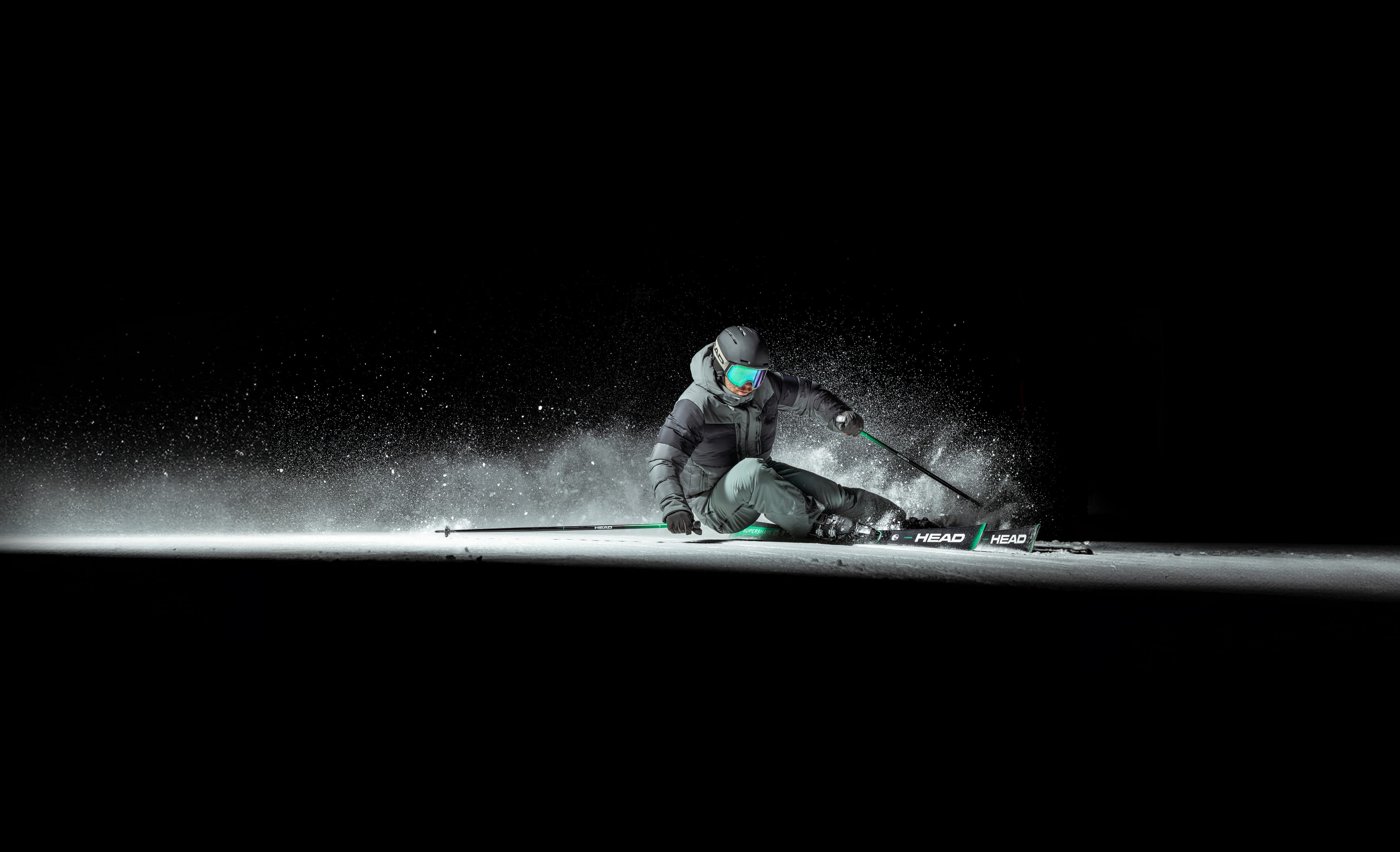 Skier in dark ski gear expertly carving a turn on a snowy slope against a black background, snow spraying dramatically.