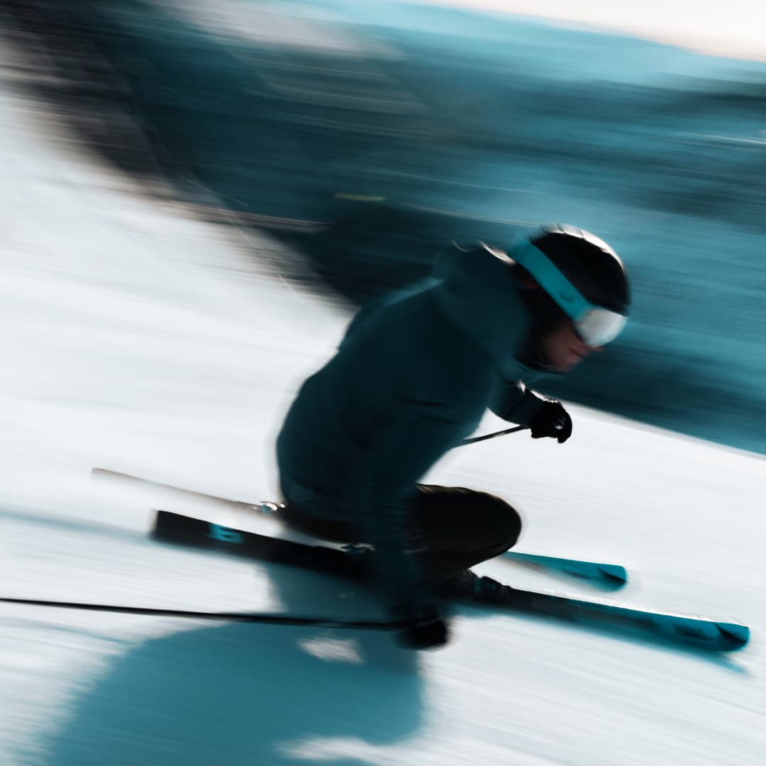 A skier in motion descends a snowy slope with blurred background indicating speed.