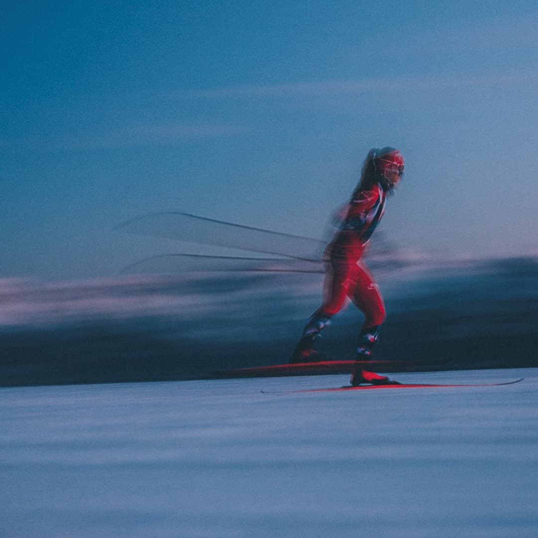 A person in red skiing swiftly on snow under a dusky sky, creating a motion blur effect.