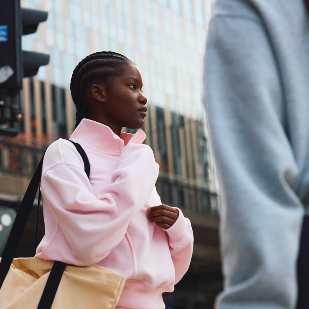 A girl in a pink sweatshirt stands on a city street.
