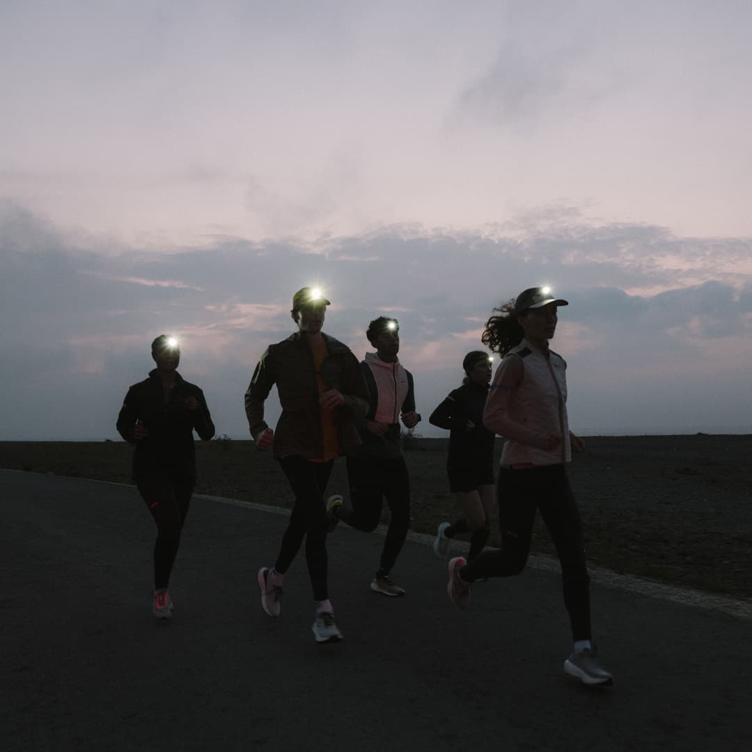 Five people runnig on a road at dusk, wearing headlamps.