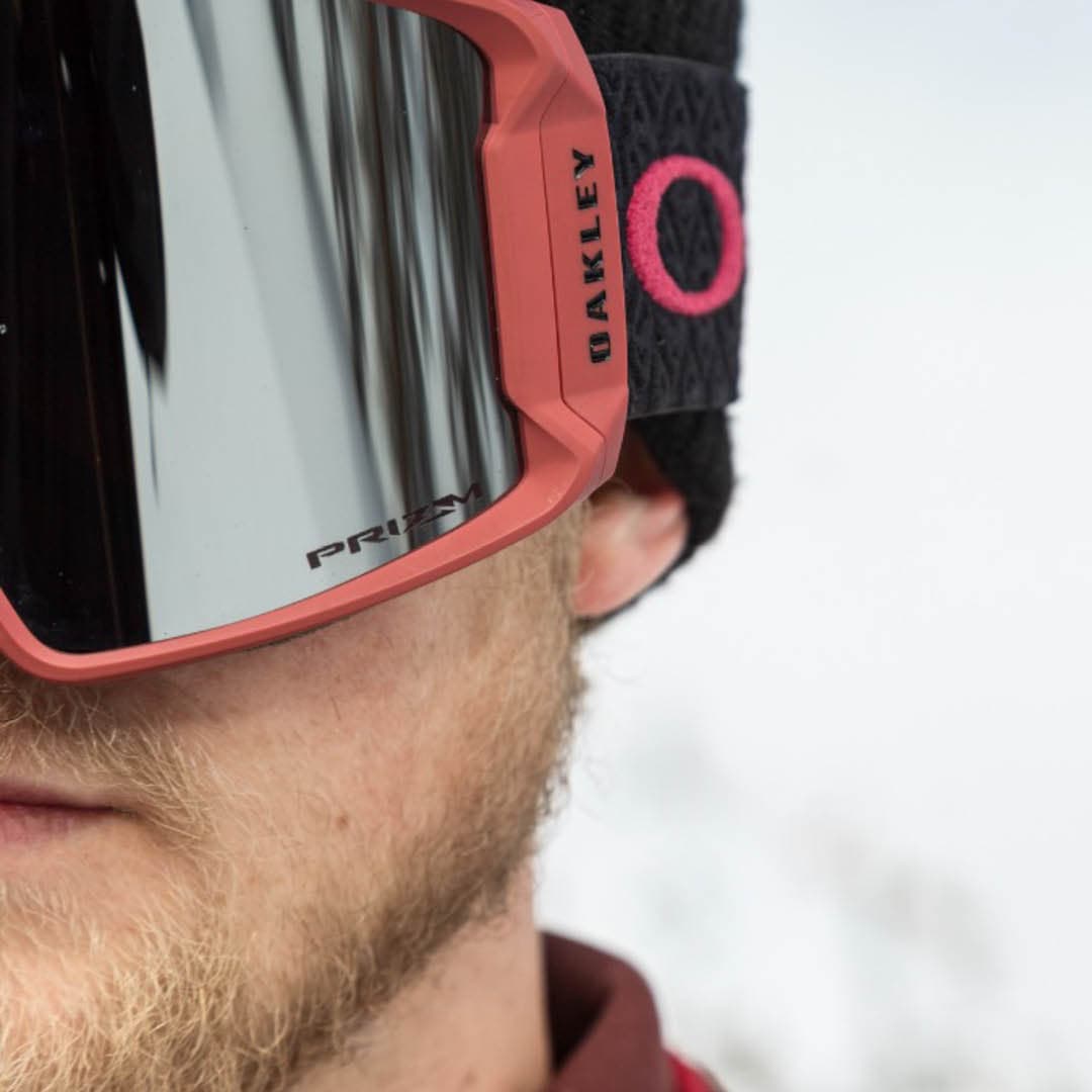 Man wearing red Oakley ski goggles with reflective lenses and a black strap.