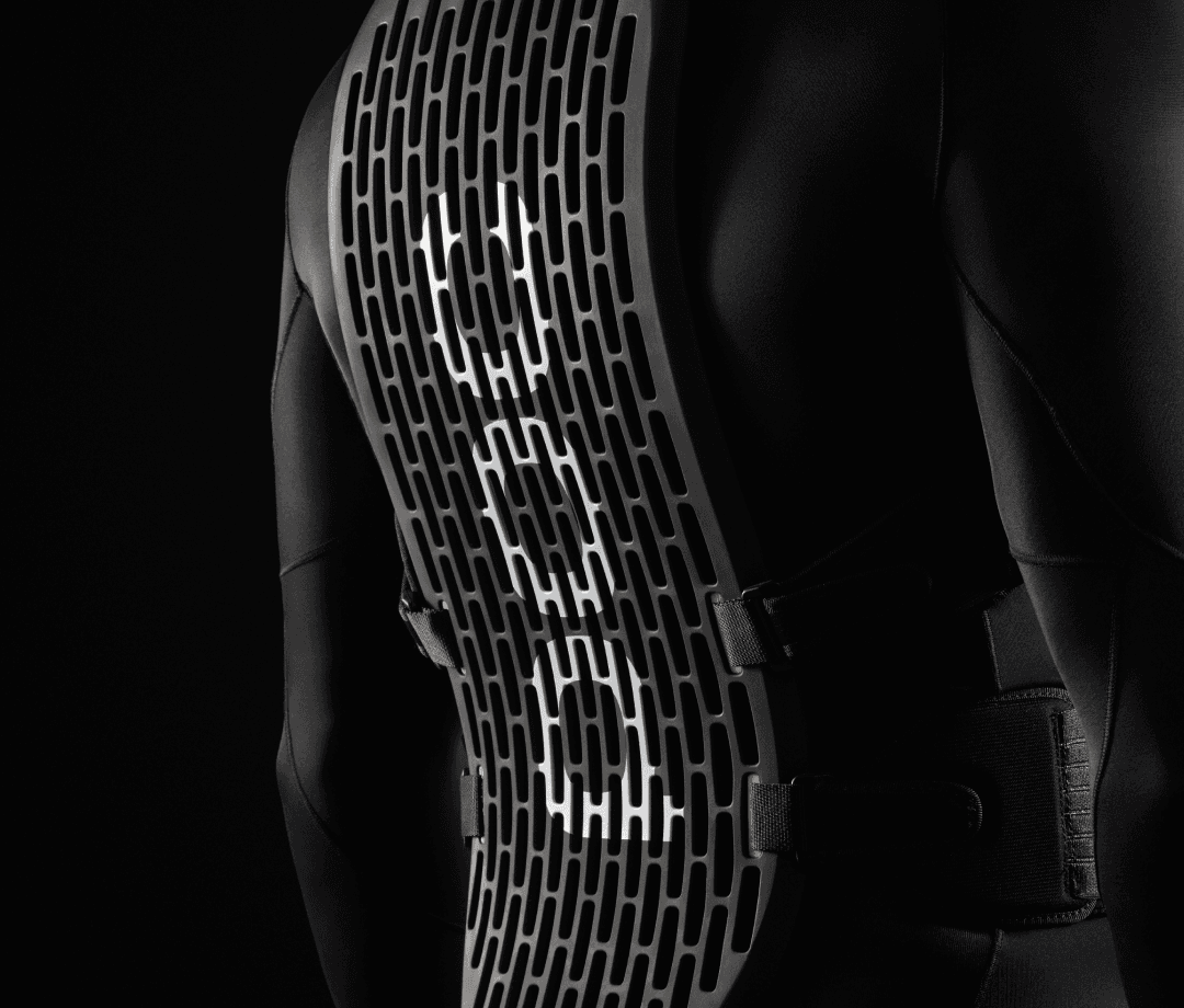 Close-up of a black protective back brace with a grid pattern, worn over a black garment, against a dark background.