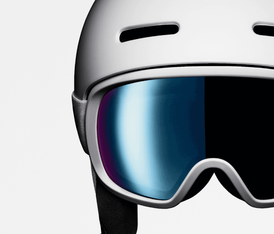 Close-up of a ski helmet with reflective goggles, showing a sleek design and a white exterior, against a plain background.