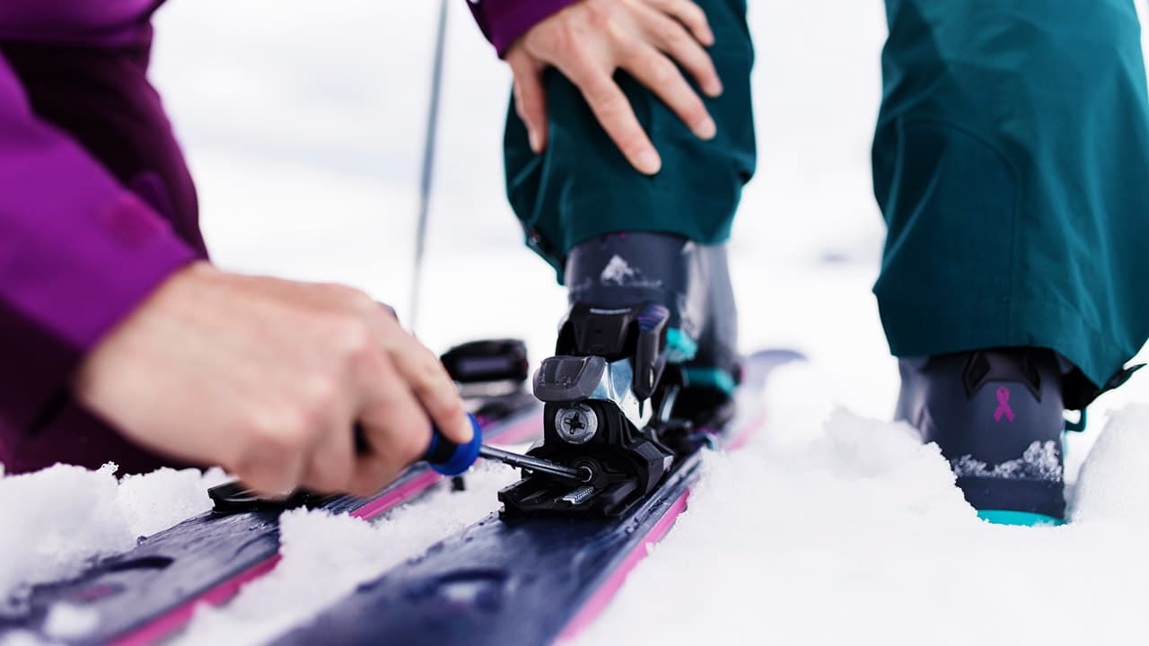 Close-up of a person adjusting a ski binding with a screwdriver.