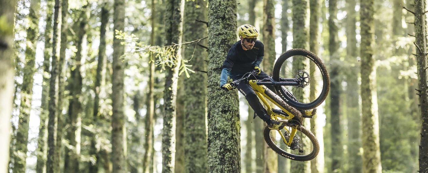 Mountain biker performing a mid-air trick in a forest.