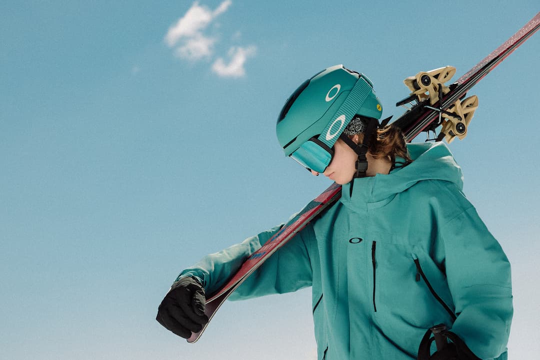 Person in Oakley clothes and gear carrying skis with a blue skye in the background