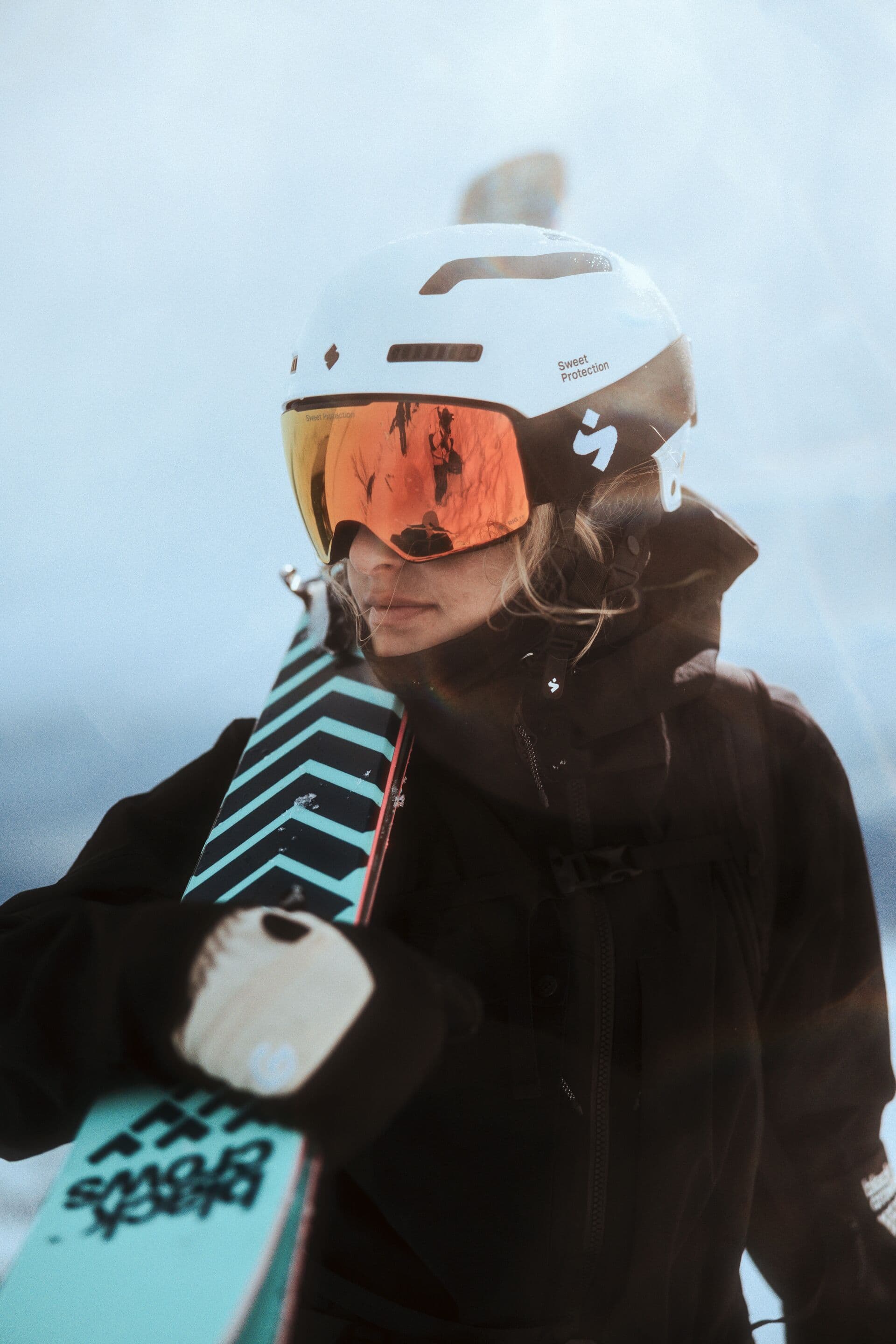 Girl wearing ski helmet and goggles, carrying a pair of skis