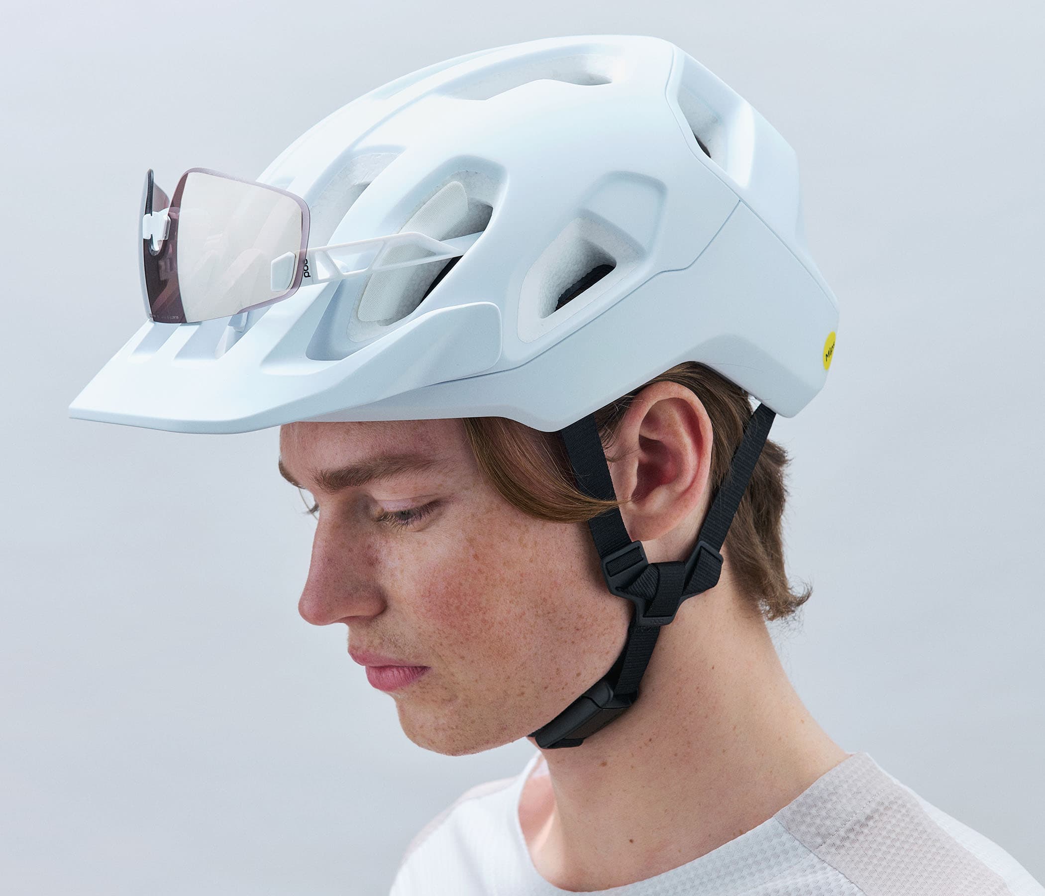 Person wearing a white bike helmet with sunglasses resting on top, against a plain background.