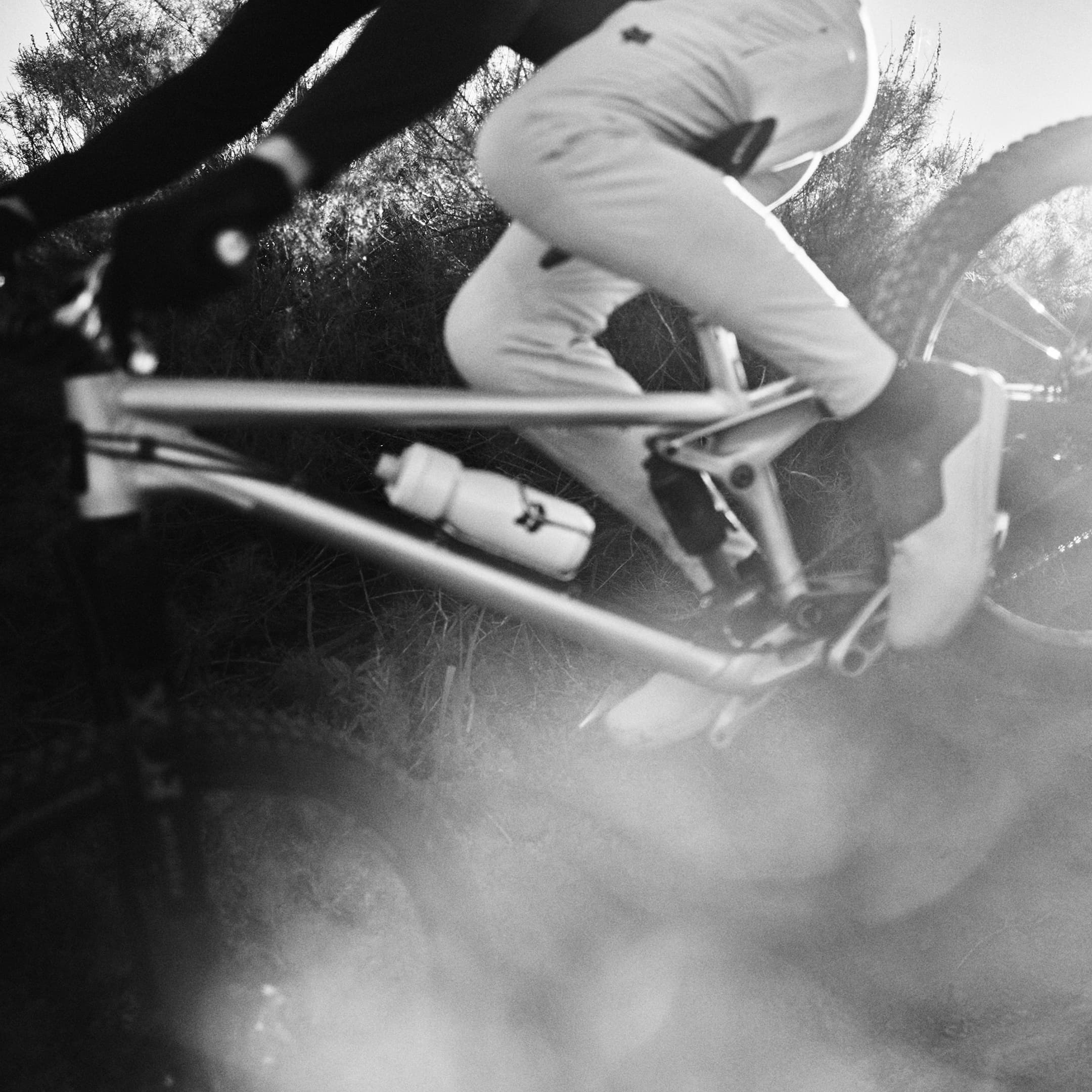 Black and white image of a cyclist riding through a sunny, dusty trail, with focus on the bike and motion blur.