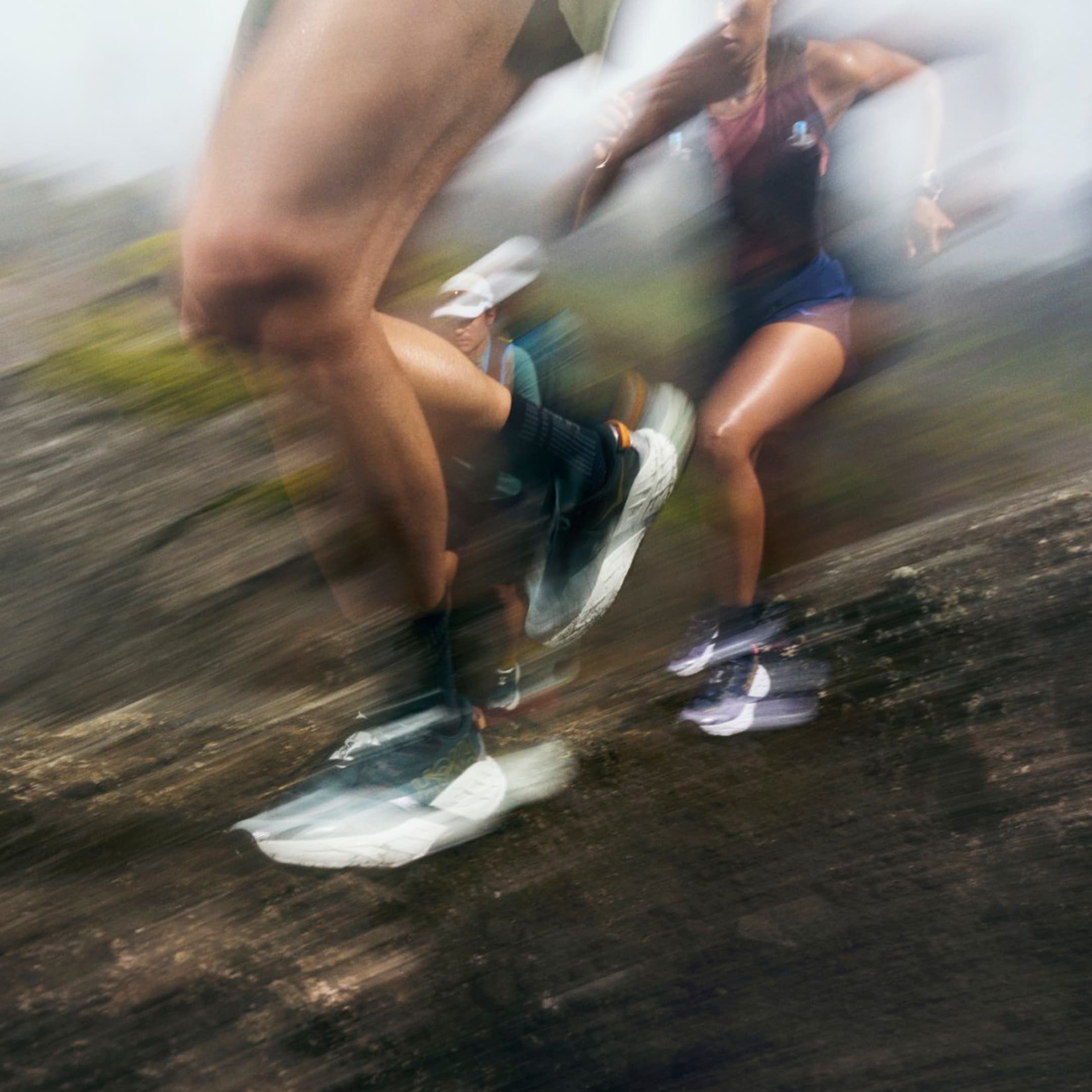 Blurred image of two people trail running on a steep, rocky slope, capturing dynamic movement and energy.