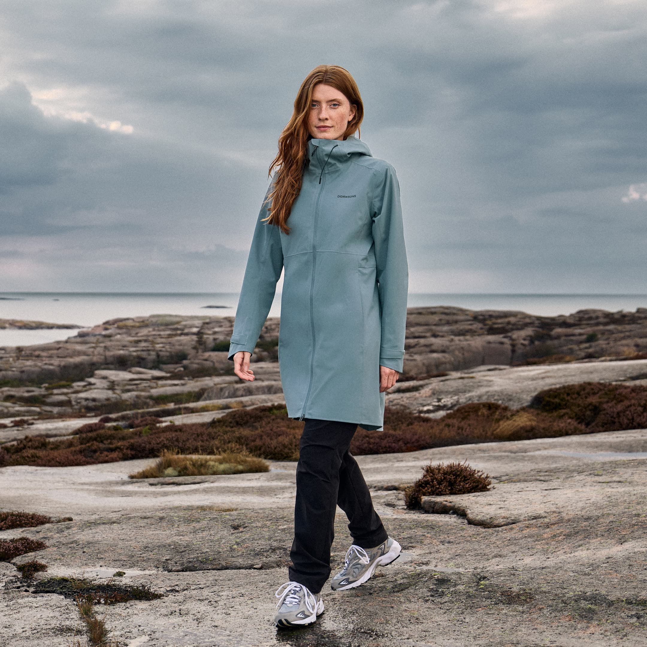 Woman in a blue Didriksons jacket on cliffs by the sea