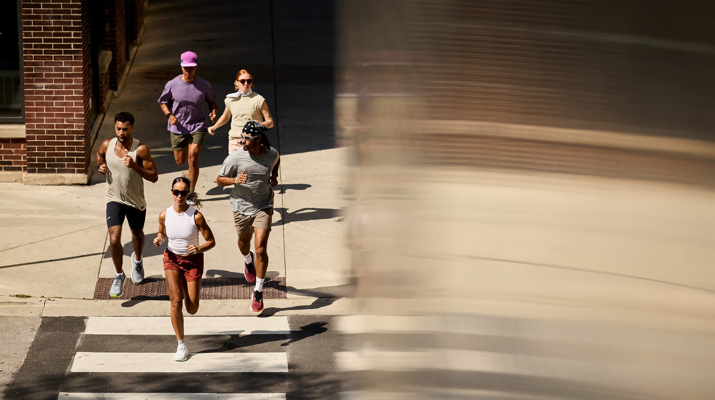 A group of five people jogging on a sunny street, casting shadows on the crosswalk.