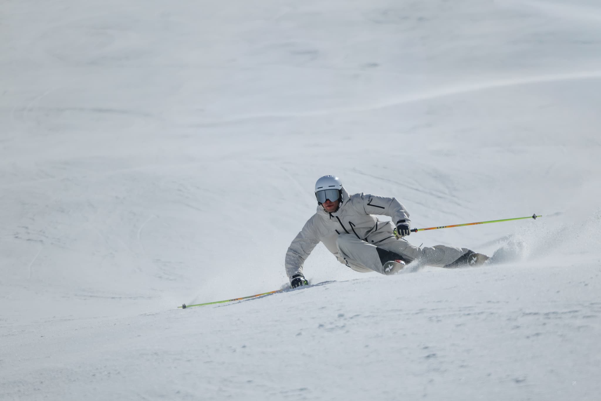 A skier in a white outfit and helmet executes a sharp turn on a snowy slope under a clear sky.
