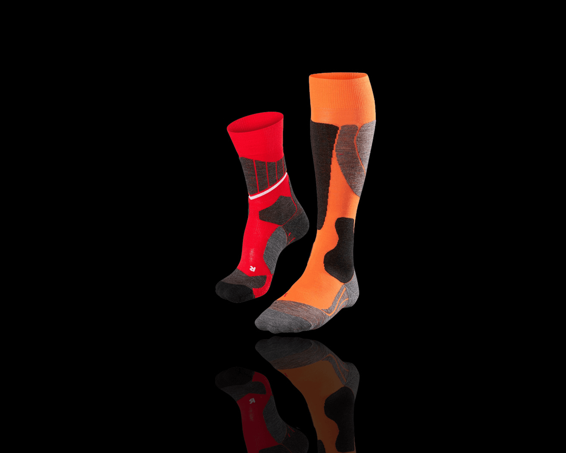 Two ski socks on a black background: one red with black and white accents, the other orange with black and gray patterns.
