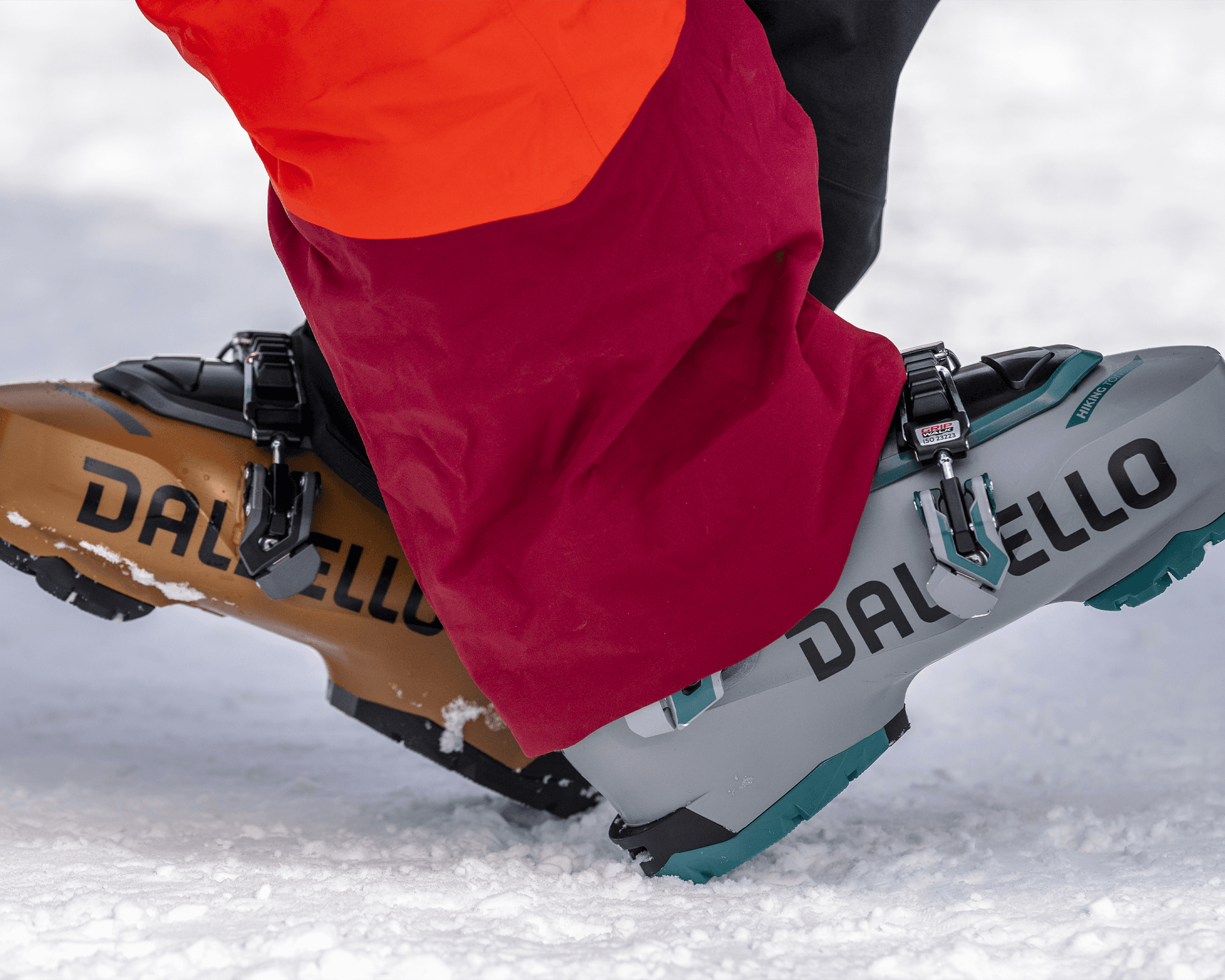 Close-up of ski boots with "Dalbello" branding, standing on snow. The boots are in gray and brown.