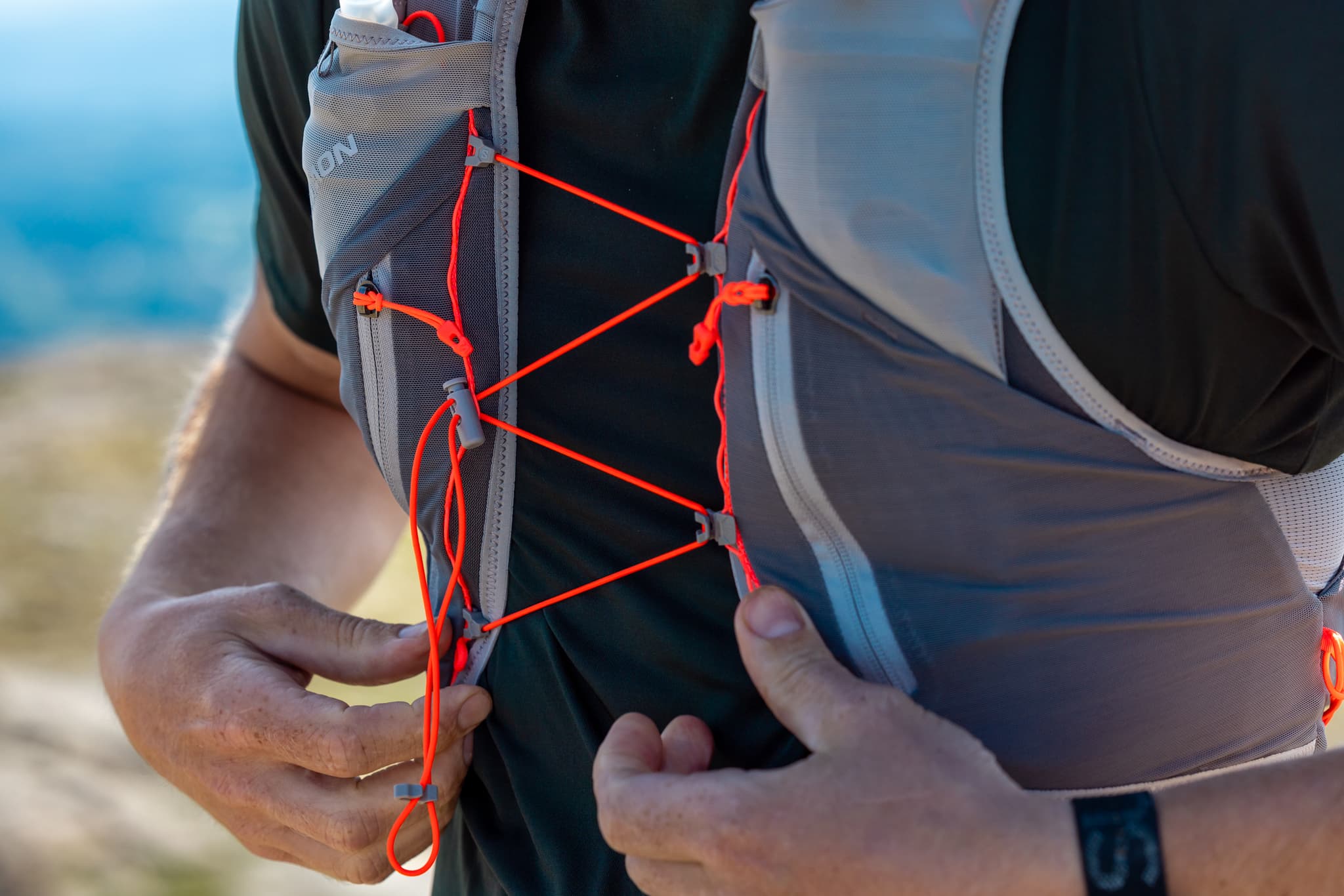 Person adjusting a gray running vest with bright orange cords.