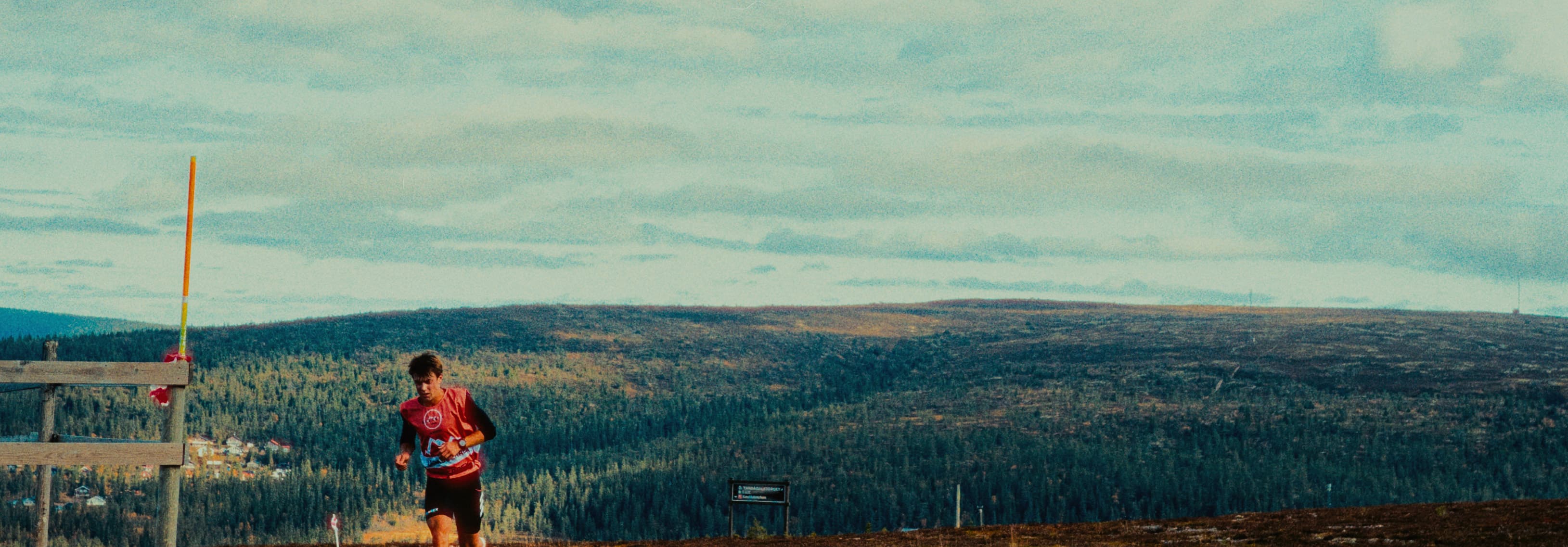 A person in a red shirt runs on a vast, open landscape with hills in the background.