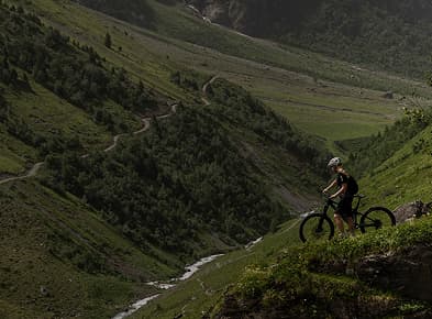Cyclist on a mountain trail, surrounded by lush green hills.