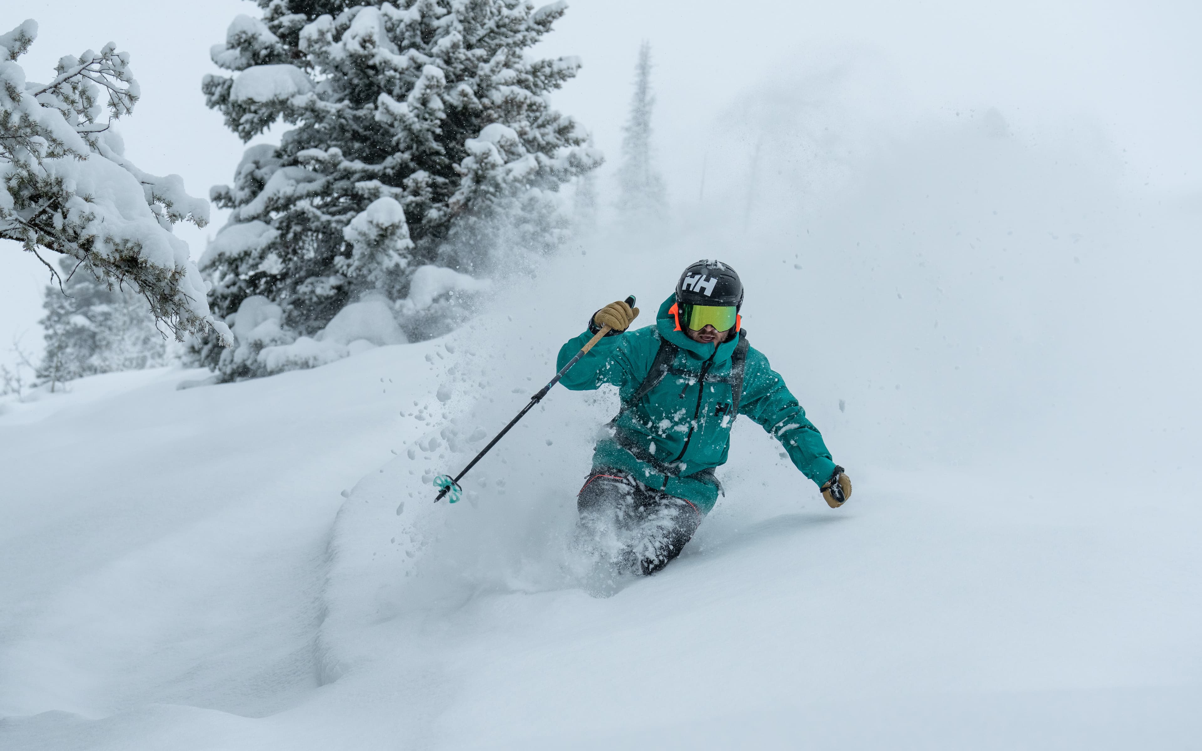 A skier in a teal jacket and helmet navigates through deep powder snow.