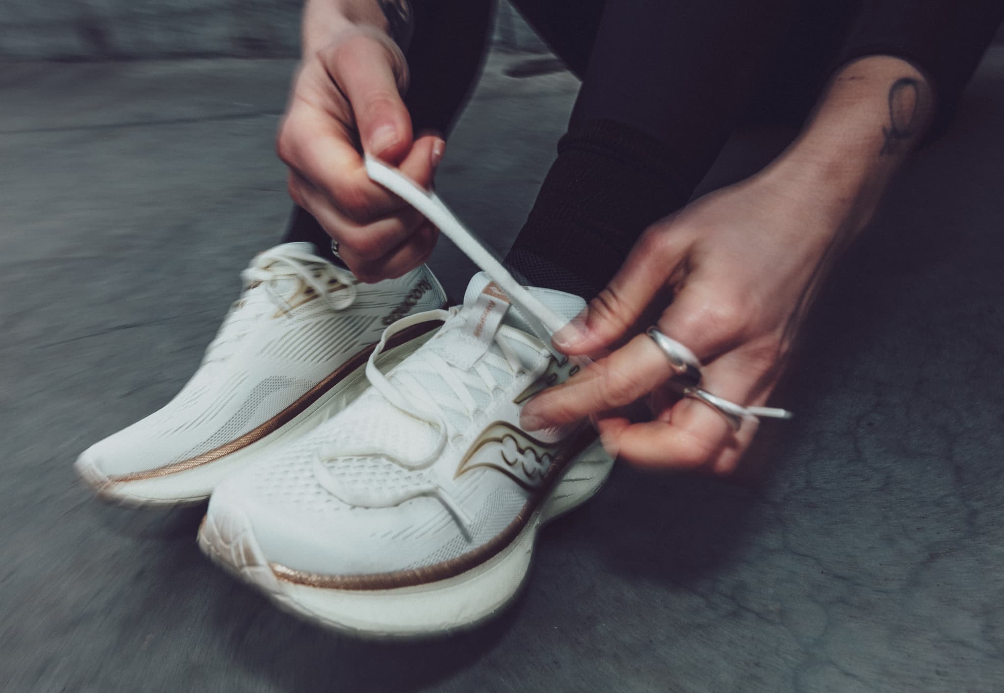 Person tying white running shoes, sitting on a concrete floor.