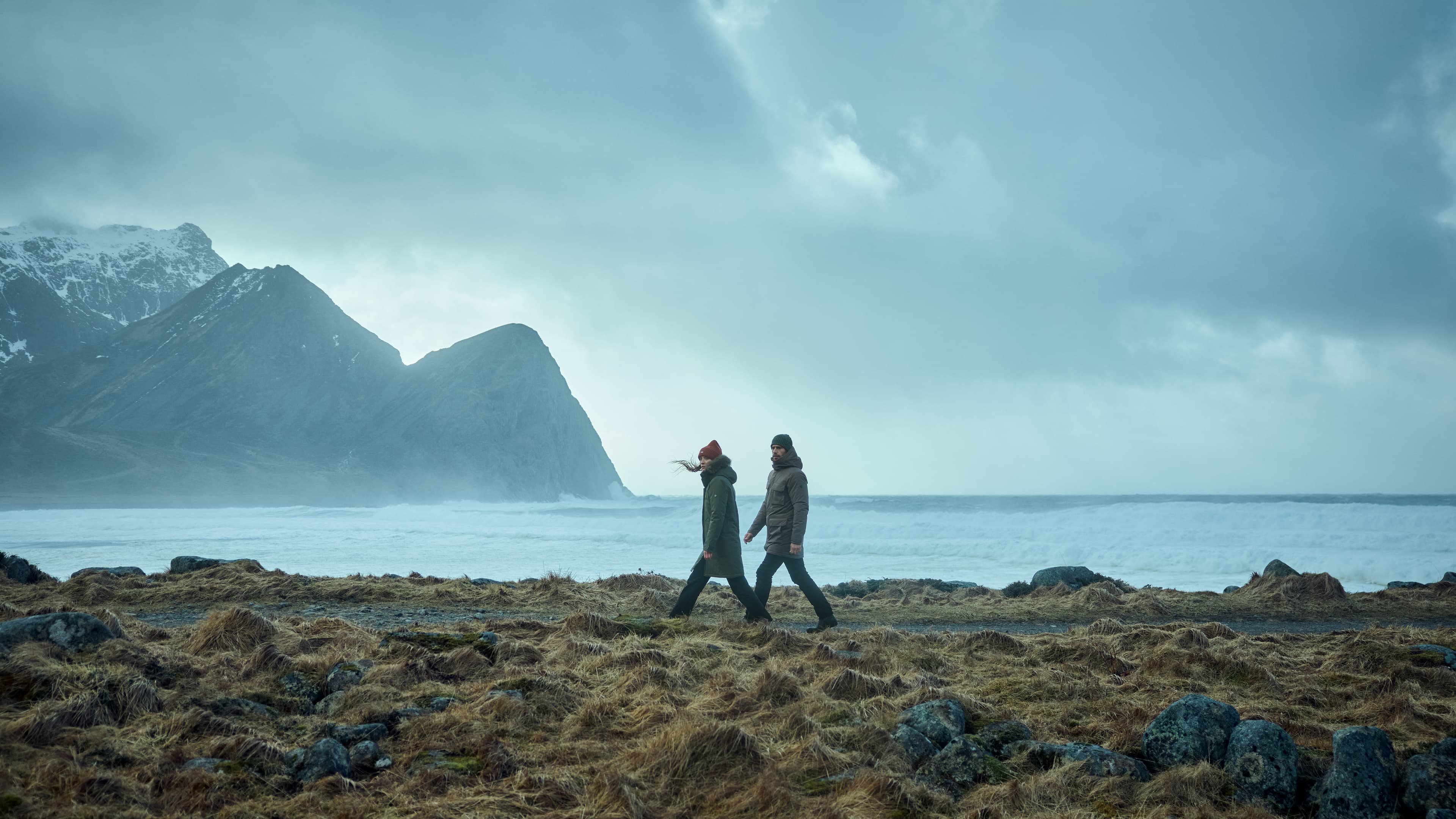 A man and a woman walking along the ocean in winter wear